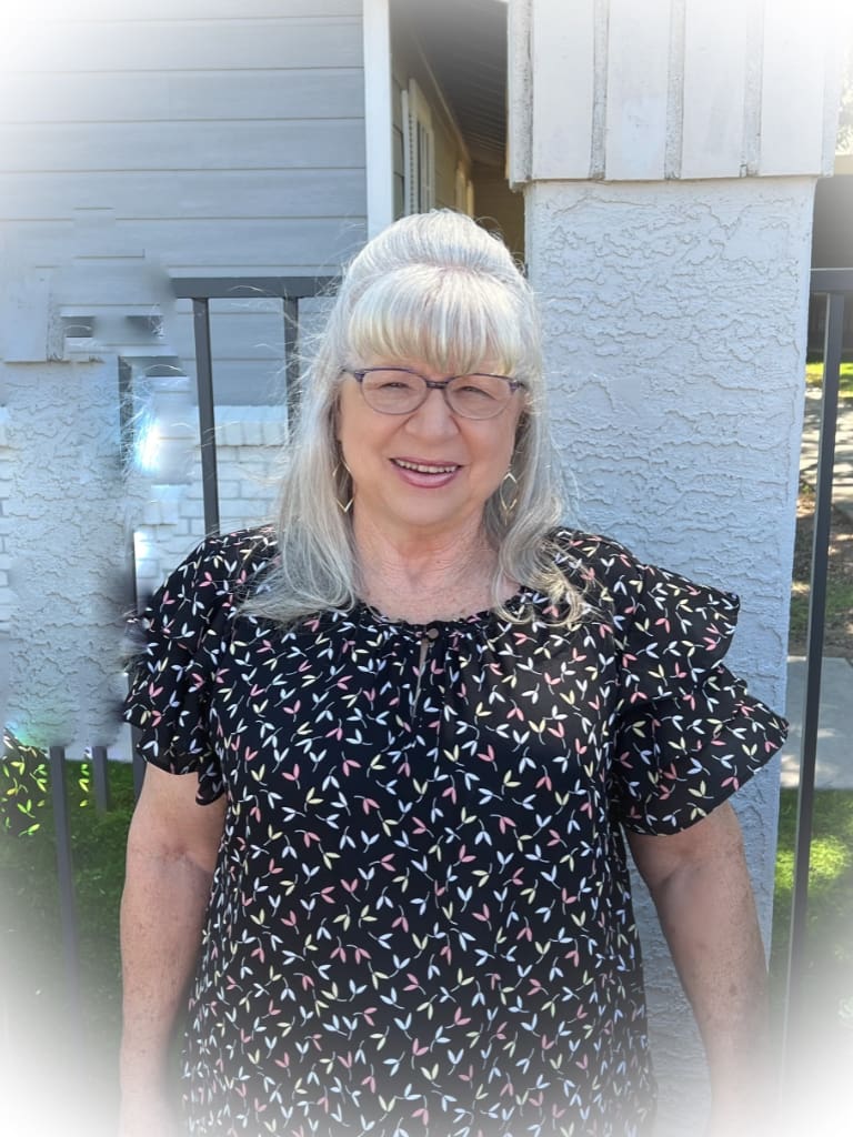 A woman with white hair and glasses standing outside.